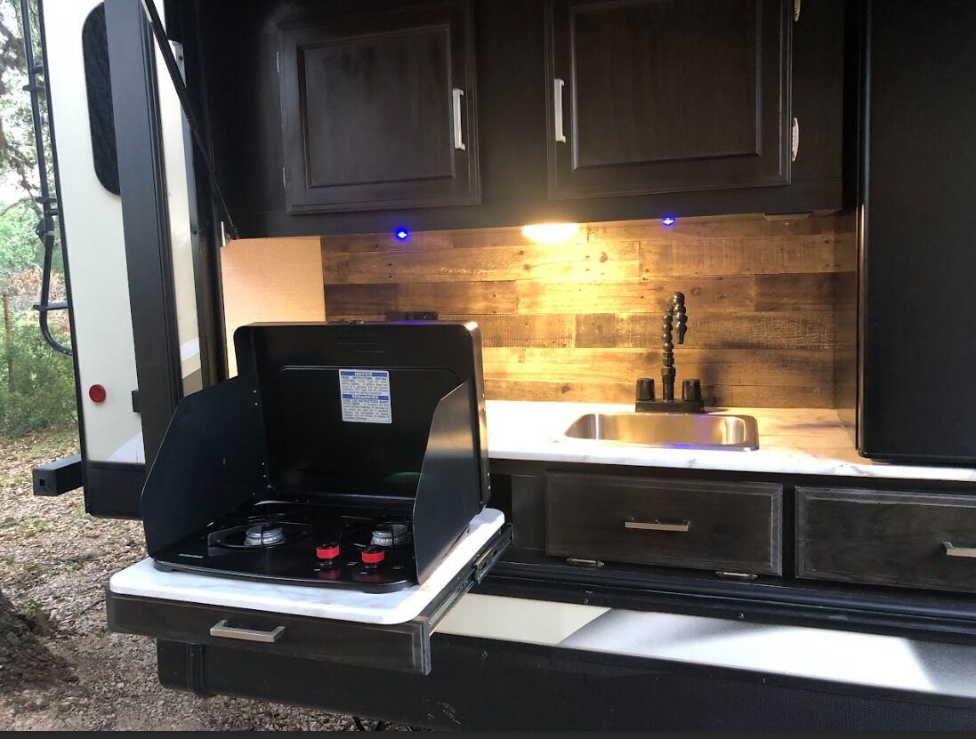 Une cuisine compacte pour camping-car, dotée d’une cuisinière intégrée, d’un évier et de meubles en bois.