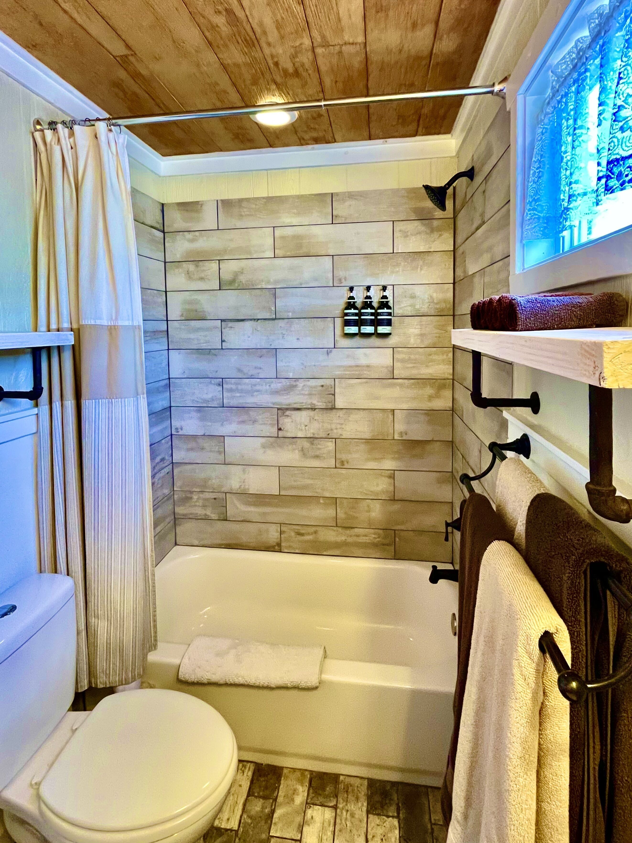 A bathroom with a wooden ceiling, a bathtub, a toilet, and a shower curtain.