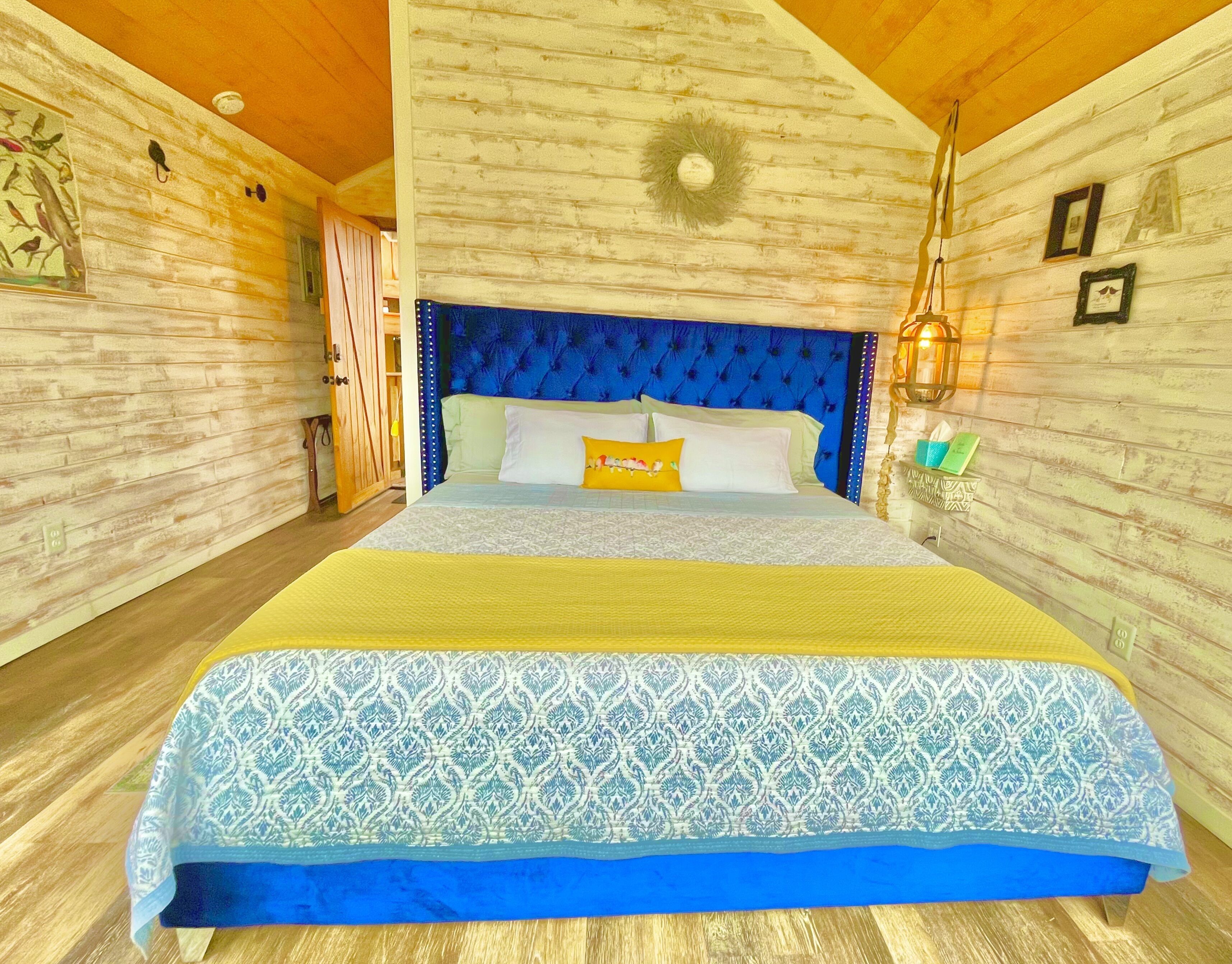 A bedroom with a large bed, a blue headboard, and a wooden ceiling.