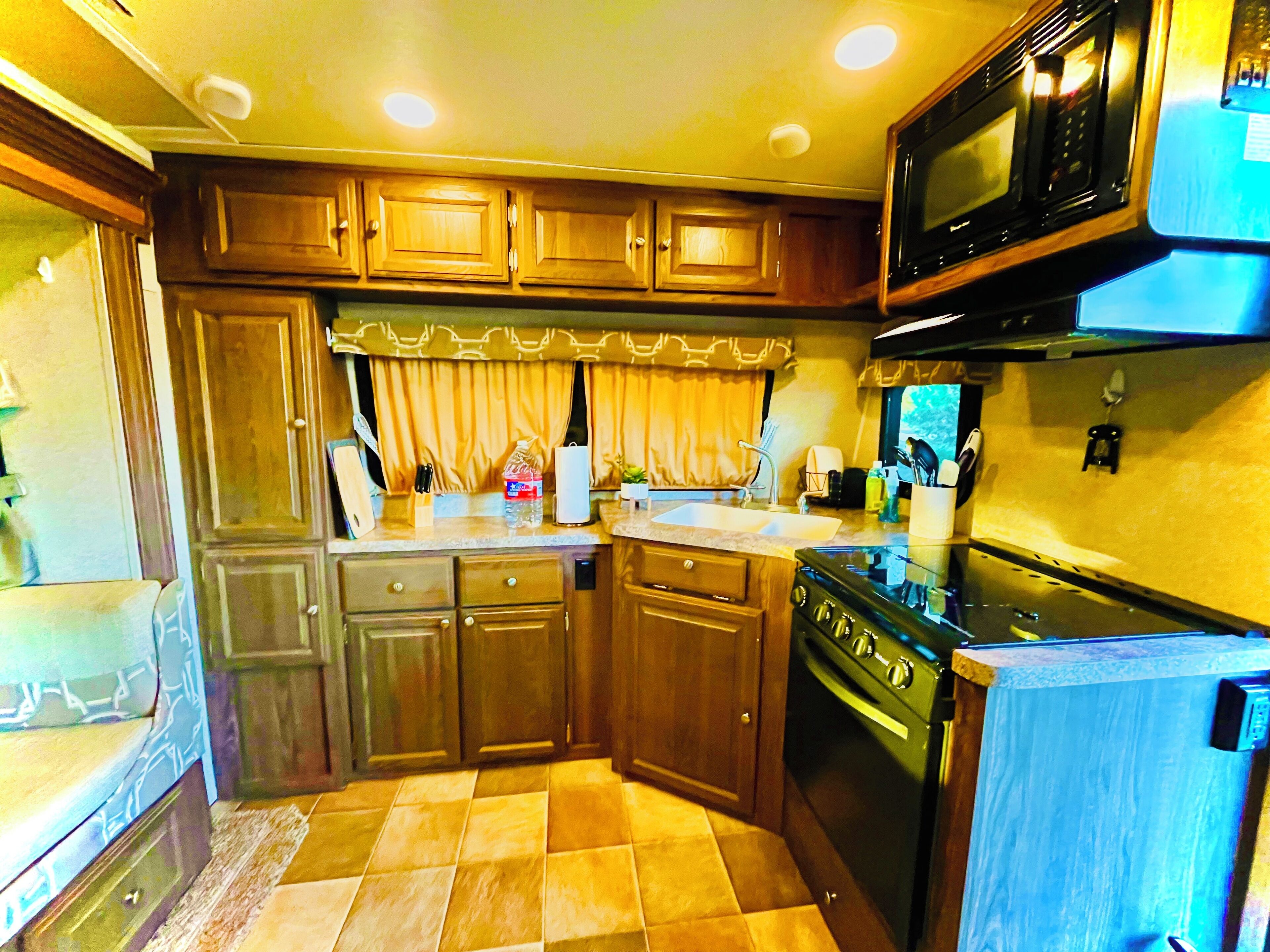 A compact kitchen with wooden cabinets, a stove, a microwave, and a sink.