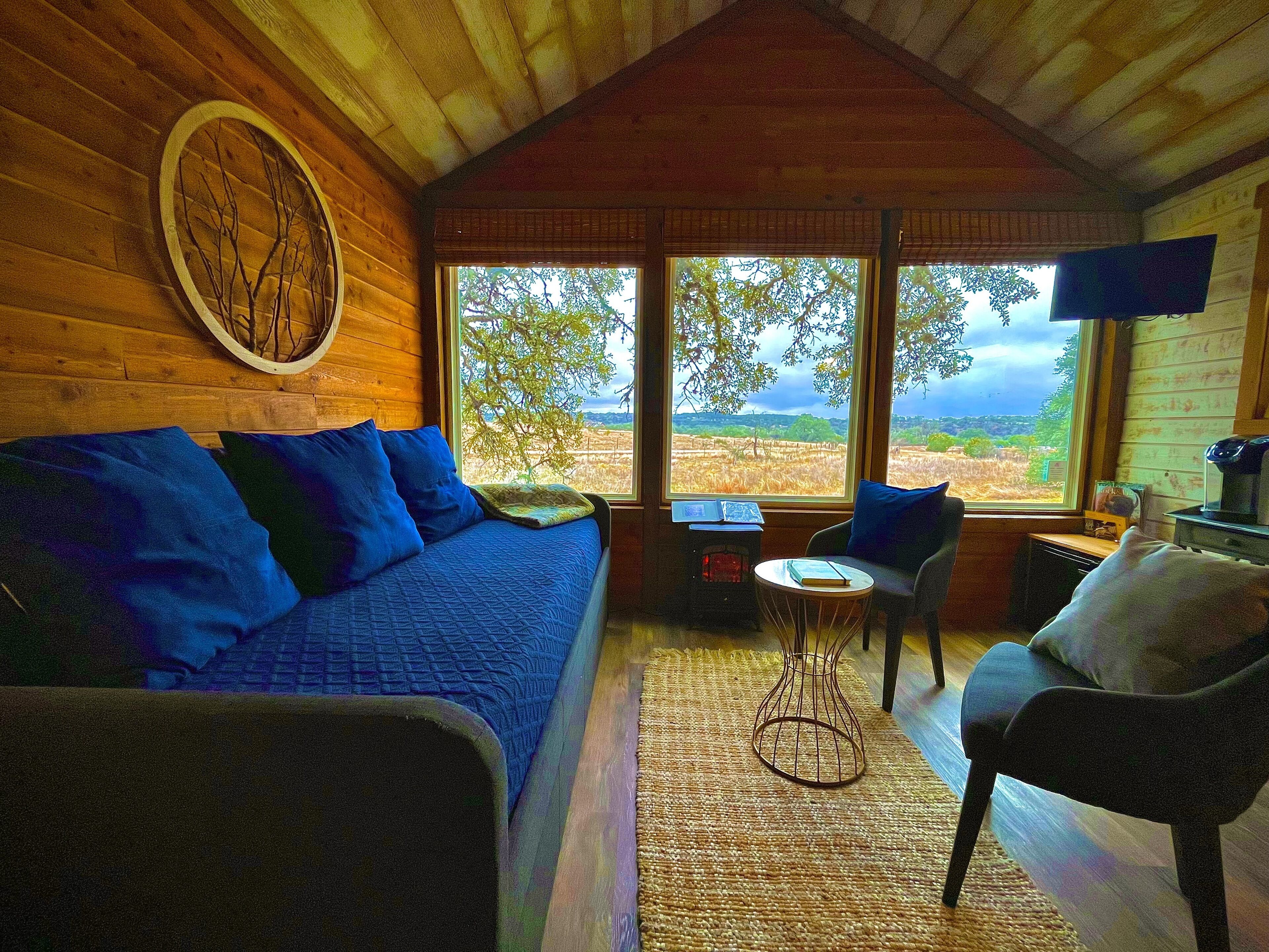 Un interior de cabaña acogedor, con techo de madera, un sofá azul, una mesita y una silla.
