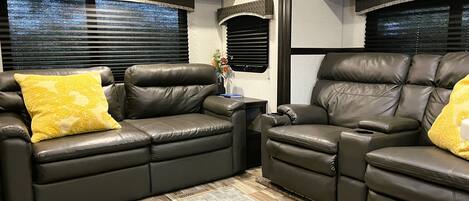 A cozy RV interior with two leather recliner sofas, a small side table, and a decorative vase.