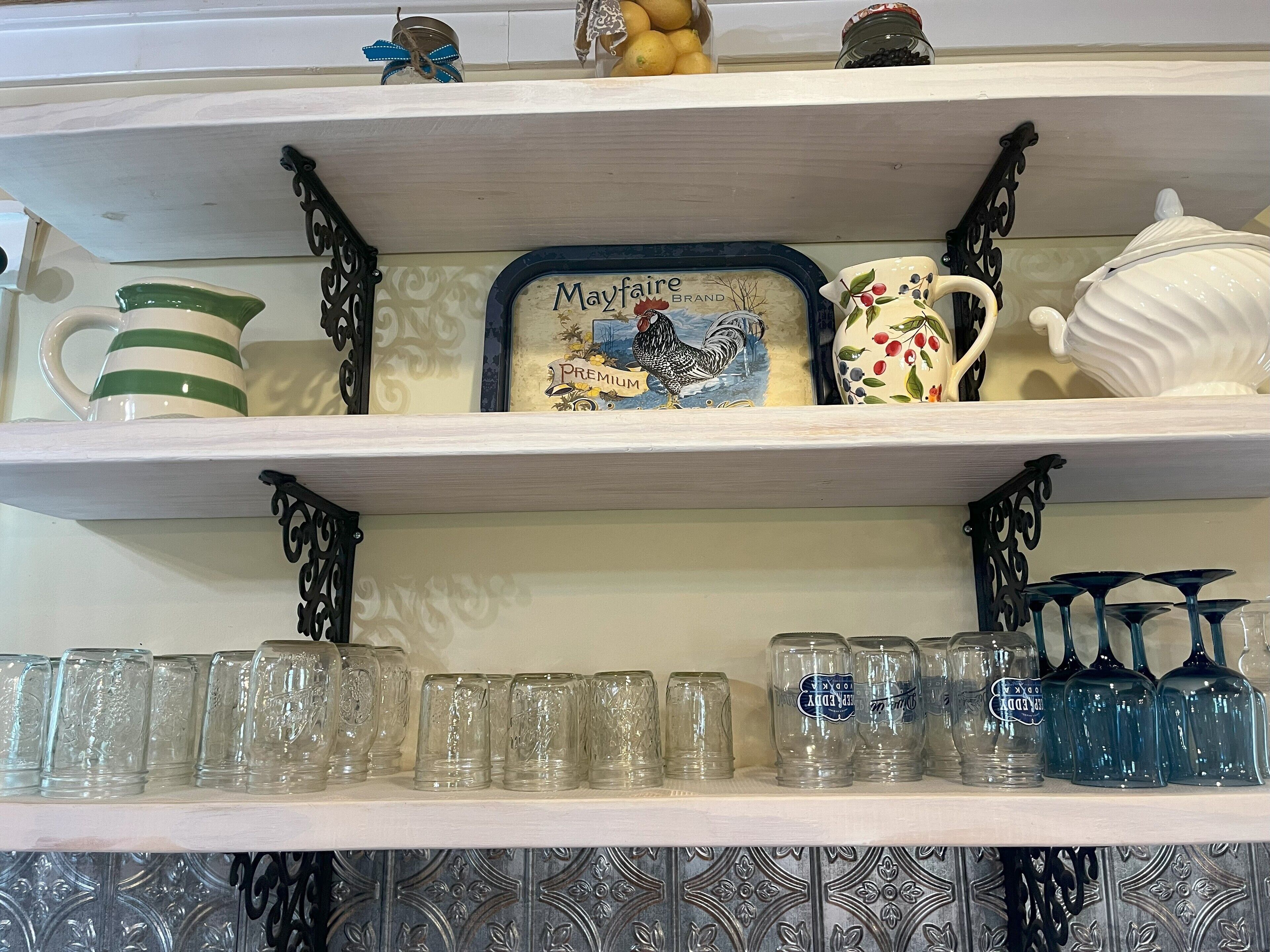 A kitchen shelf with decorative items, including a Mayfaire brand mug, a ceramic rooster, and a white teapot.