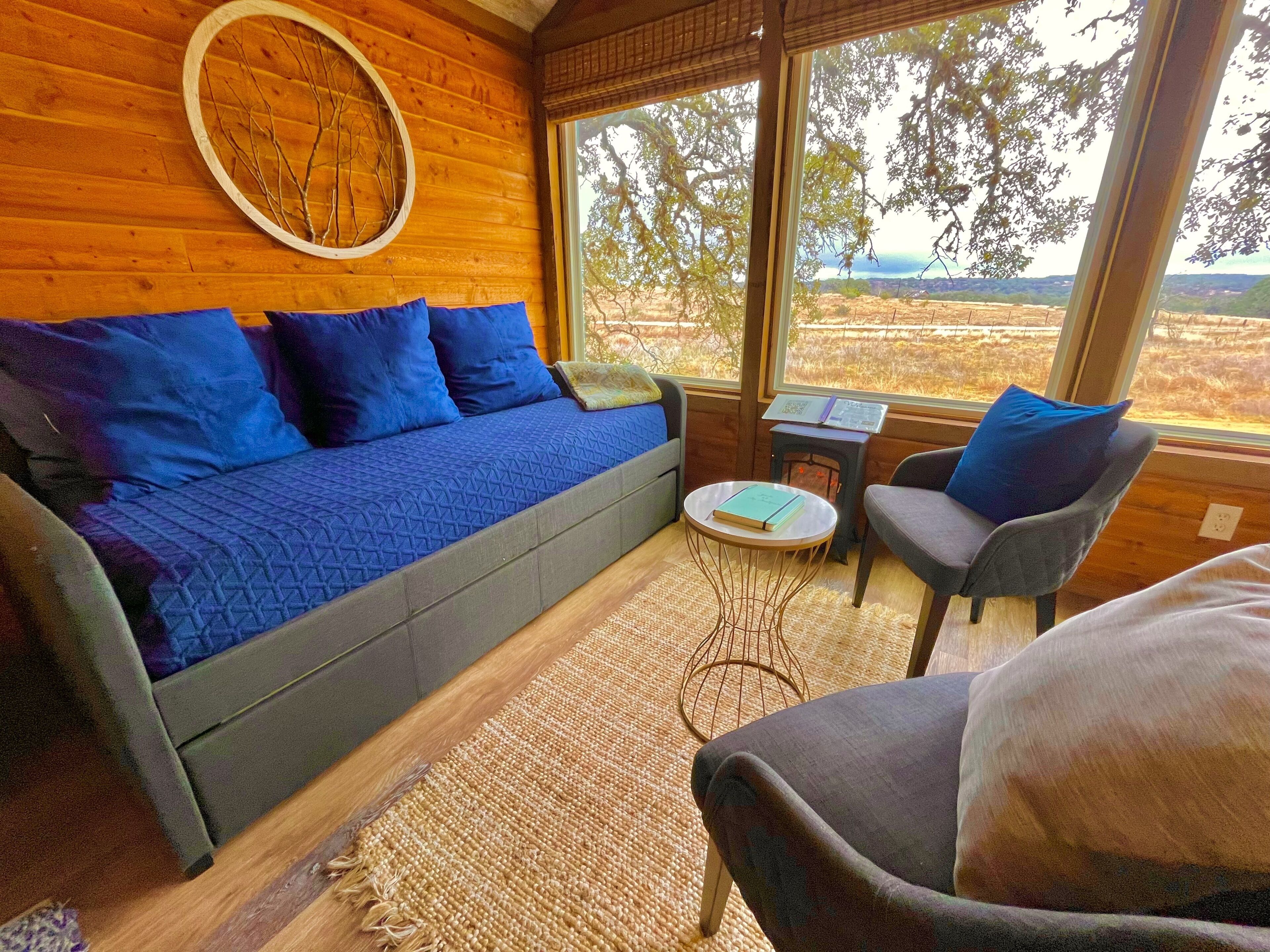 Une pièce chaleureuse avec un mur en bois, un canapé bleu agrémenté de coussins, une petite table ronde sur laquelle repose un livre, et une chaise.