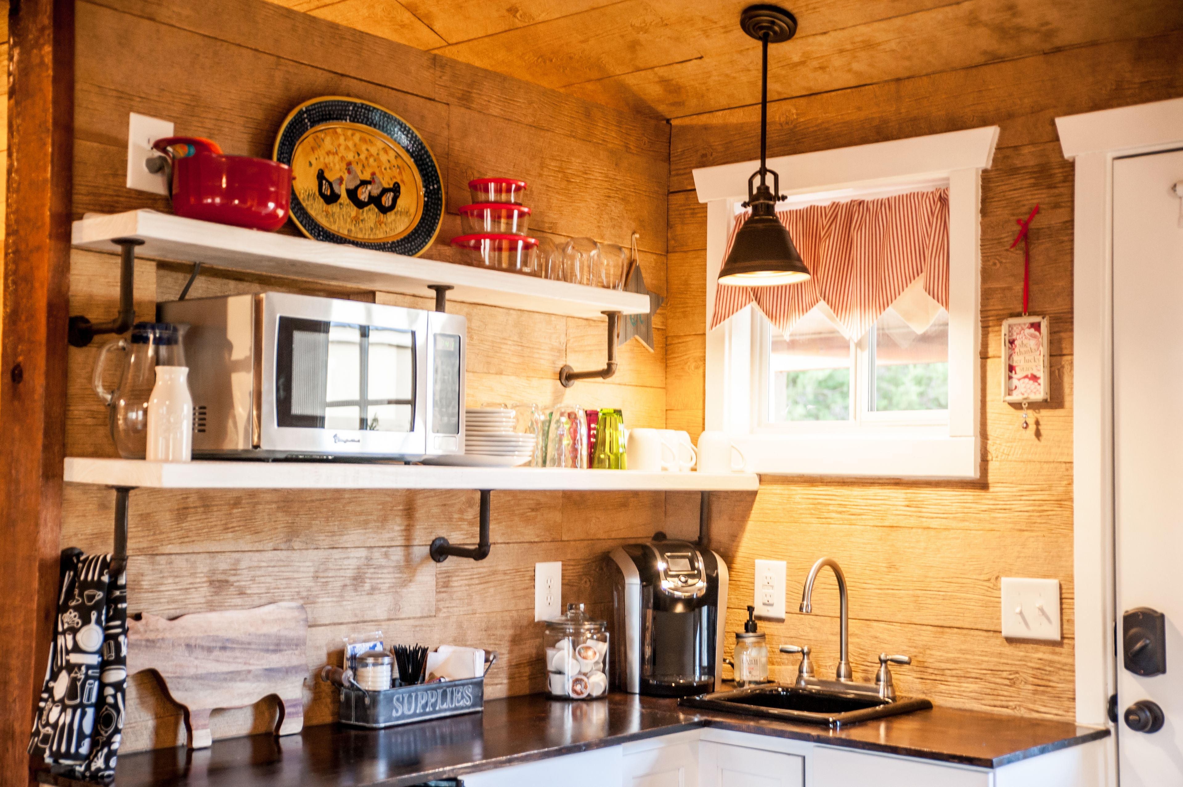 A kitchen with wooden walls, a white microwave, a coffee maker, and a window with striped curtains.