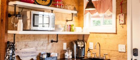 A kitchen with wooden walls, a white microwave, a coffee maker, and a window with striped curtains.
