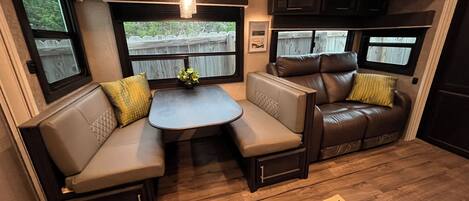 A compact RV interior with a seating area, a small table, and a ceiling light fixture.