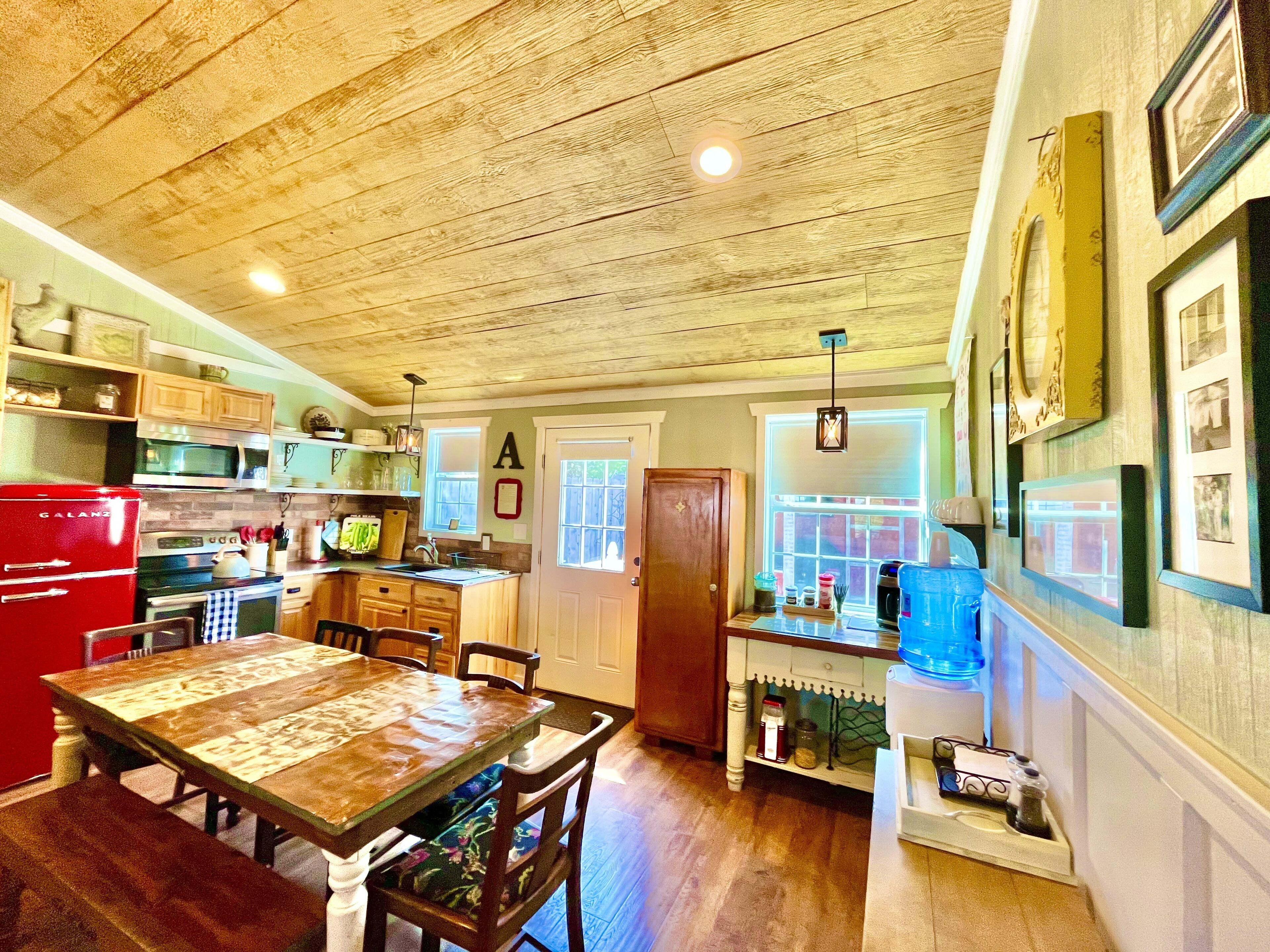A kitchen with wooden cabinets, a red refrigerator, a dining table with chairs, and a window with a view of the outside.