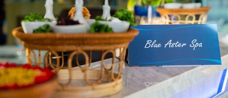 Een receptie met een bord waarop 'Blue Aster Spa' staat en een decoratieve presentatie van eten en kaarsen.
