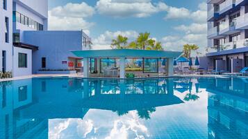 A modern hotel with a large swimming pool, palm trees, and a clear blue sky.