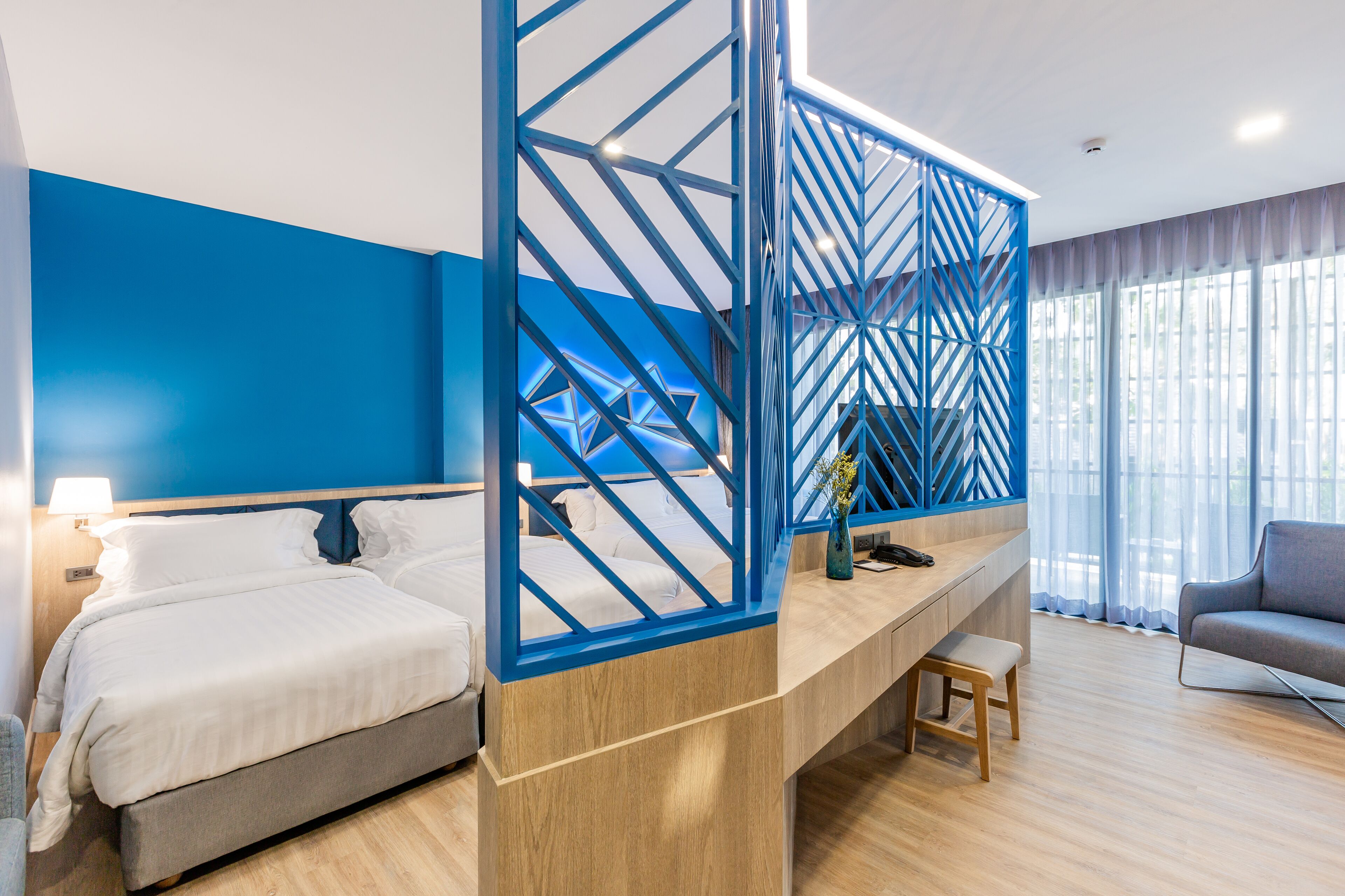 A modern hotel room with a bed, a desk, and a seating area.