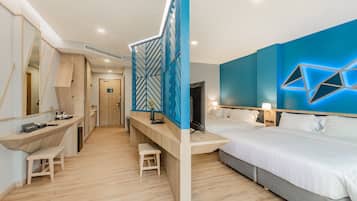 A modern hotel room with a wooden desk, two single beds, a large mirror, and a geometric light fixture on the wall.