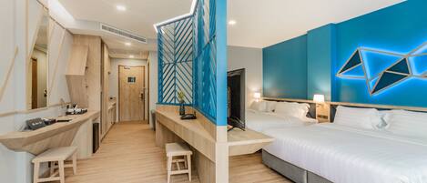 A modern hotel room with a wooden desk, two single beds, a large mirror, and a geometric light fixture on the wall.