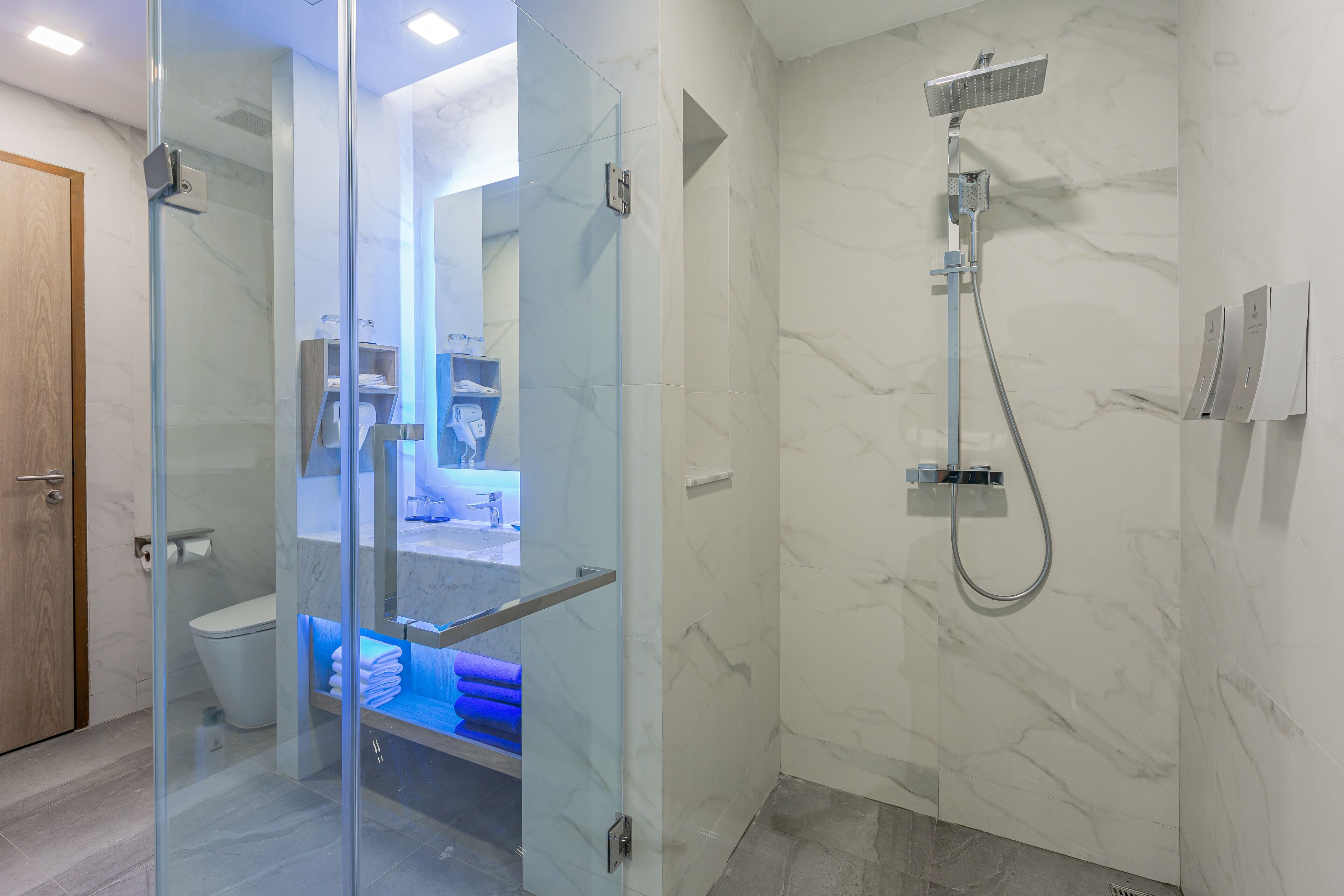 Een moderne badkamer met een douche met glazen wand, een marmeren wand en een zichtbaar toilet.