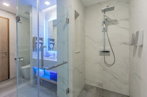 Een moderne badkamer met een douche met glazen wand, een marmeren wand en een zichtbaar toilet.