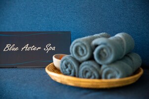 Een bord met de tekst 'Blue Aster Spa' naast een houten schaal met opgerolde handdoeken.