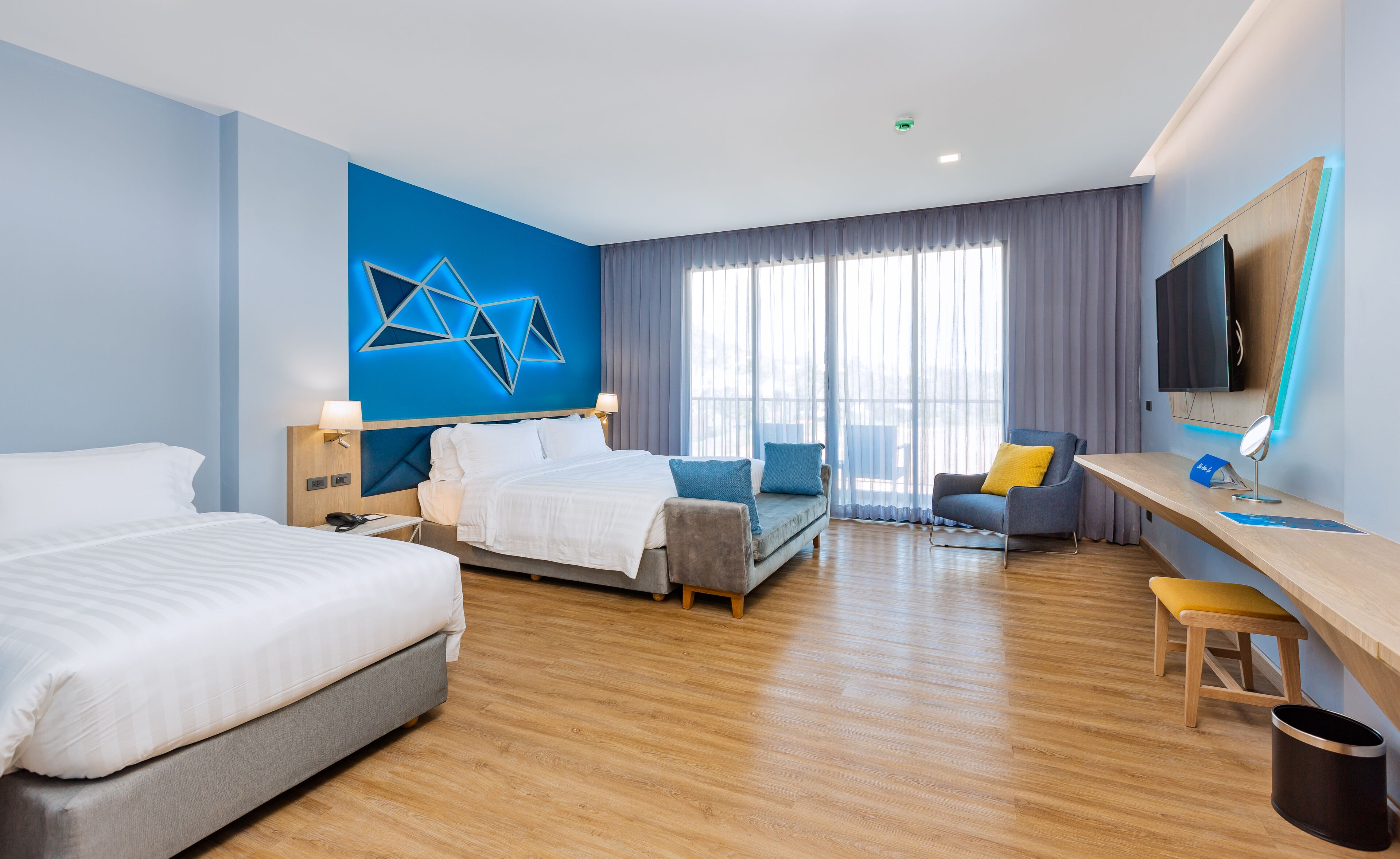 Een hotelkamer met twee bedden, een bureau, een stoel, een televisie en een groot raam met gordijnen.