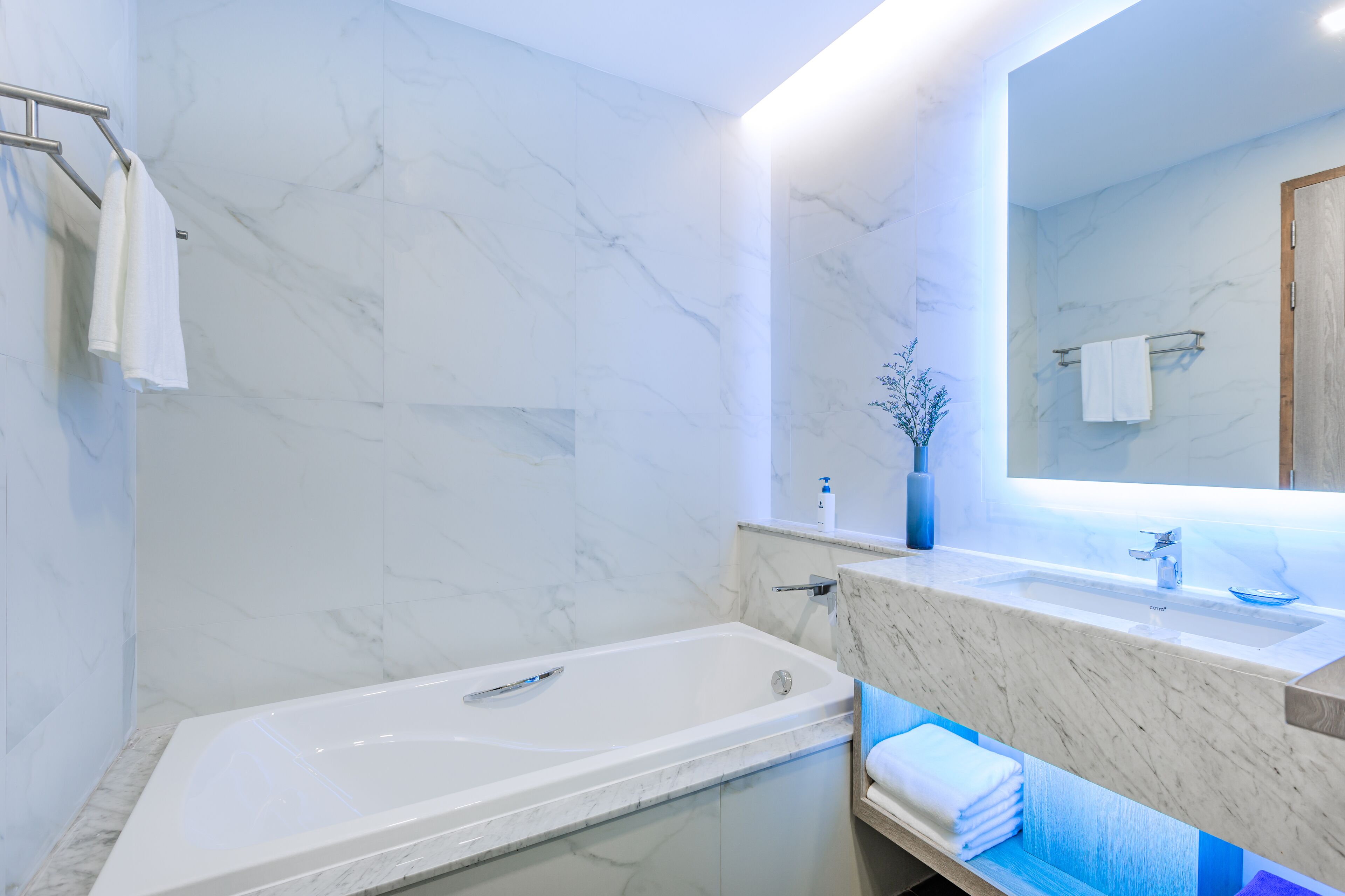 A modern bathroom with a marble wall, a bathtub, a sink, and a mirror.