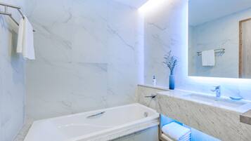 A modern bathroom with a marble wall, a bathtub, a sink, and a mirror.