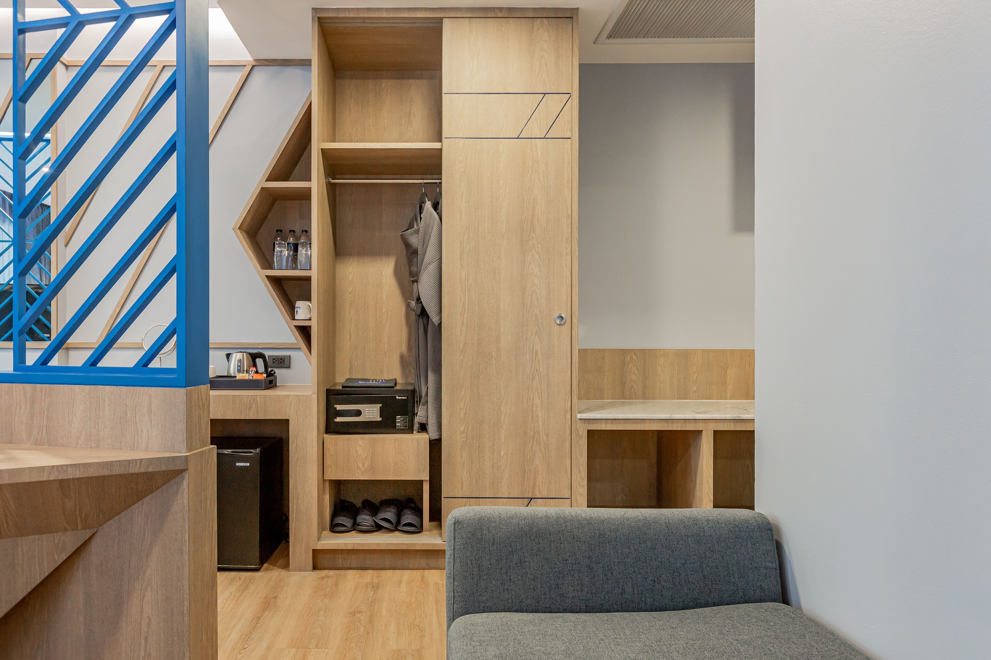 A compact room with a built-in wardrobe, a small seating area, and a staircase with blue railings.
