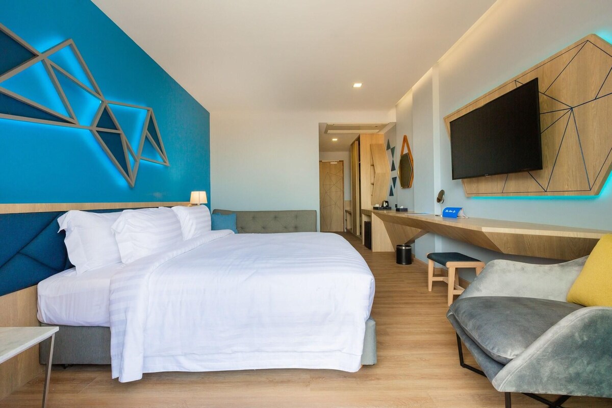 Una habitación de hotel moderna con una cama grande, un escritorio, un televisor y una zona de estar.
