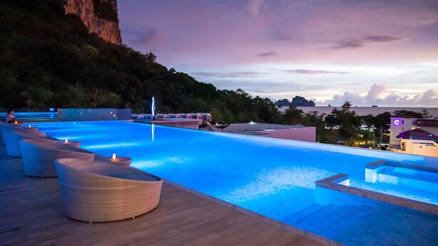 A swimming pool with lounge chairs, a wooden deck, and a view of a cliff and distant landscape.