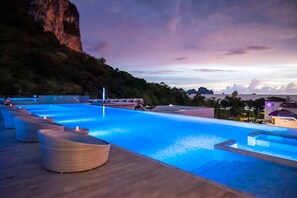 Una piscina con sillones de descanso, una terraza de madera y vistas a un acantilado y un paisaje lejano.