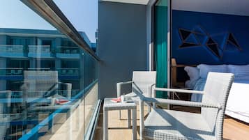 Un balcon avec des fauteuils en osier, une petite table et un lit adossé à un mur bleu, décoré de motifs géométriques.