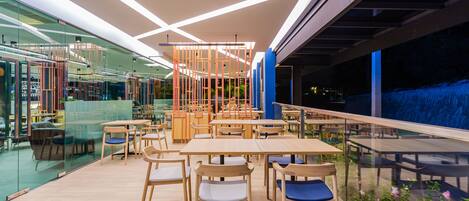 A modern indoor dining area with wooden tables and chairs, glass partitions, and a view of the outside.