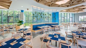 A modern restaurant with wooden furniture, blue accents, and large windows offering a view of palm trees.