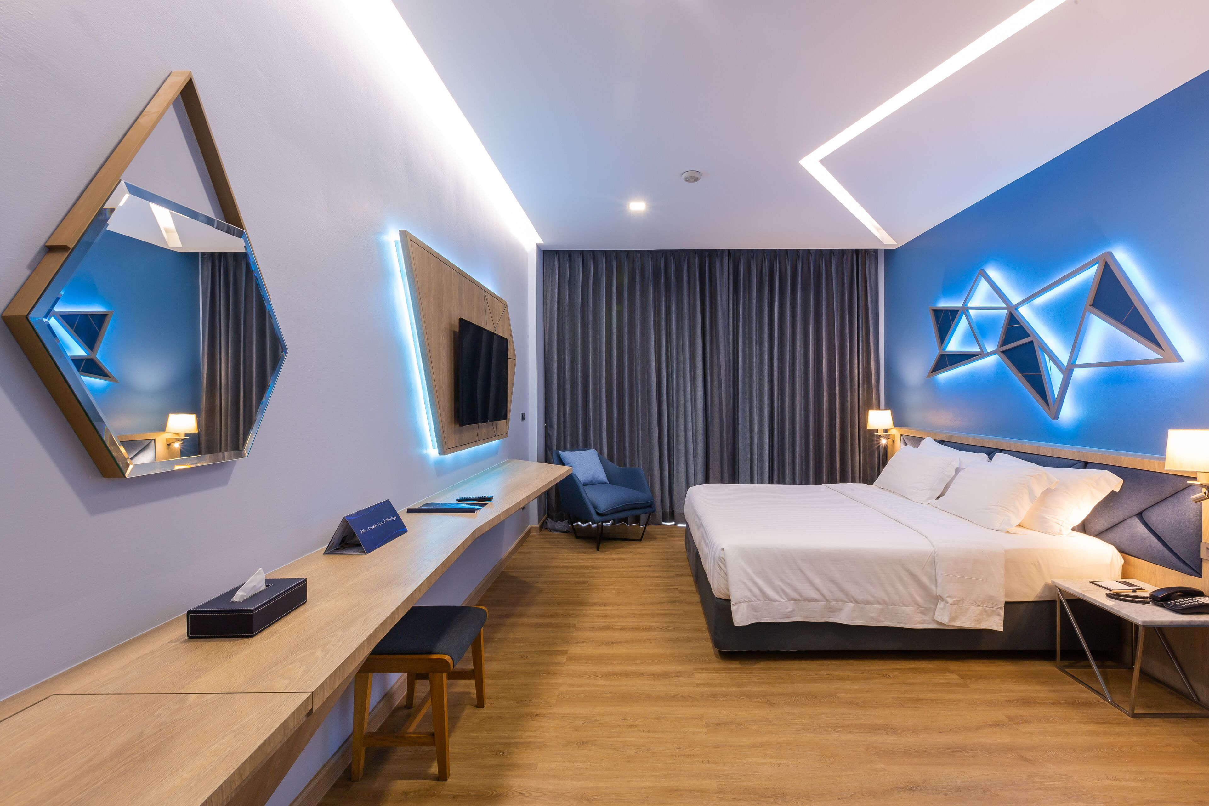 A modern hotel room with a bed, desk, chair, and a large mirror.