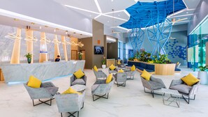 A modern lobby with a reception desk, seating area, and a blue geometric ceiling structure.
