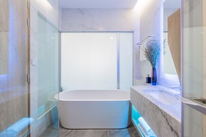 Een moderne badkamer met een vrijstaand bad, een douchecabine van glas en marmeren aanrechtbladen.