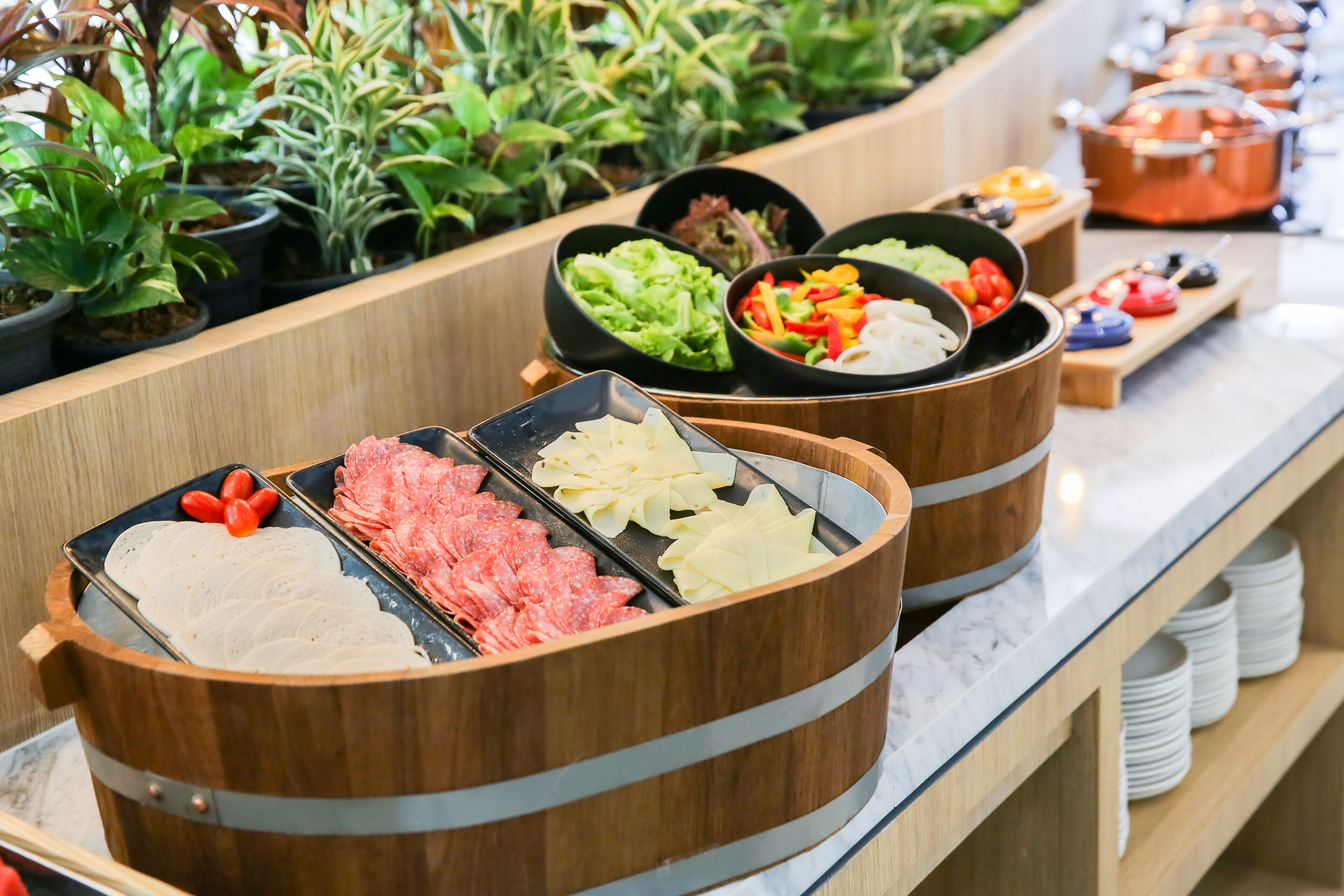 Un bufé con diversos alimentos, incluyendo carnes, verduras y salsas en recipientes de madera.