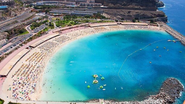 A coastal resort with a large sandy beach, a swimming area, and buildings on a cliff overlooking the sea. - Ocean view apartment in Playa del Cura Gran Canaria (Mogán)