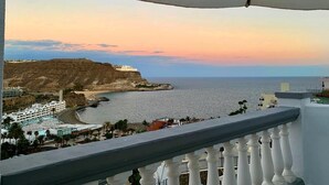 A coastal view from a balcony with a white railing, overlooking a beach, a cliff, and a resort area. - Ocean view apartment in Playa del Cura Gran Canaria (Mogán)
