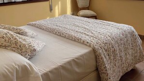 Une chambre avec deux lits, une chaise, une étagère avec des objets décoratifs et un luminaire au plafond.