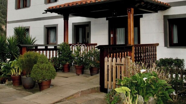 Un bâtiment à deux étages, doté d’un toit en tuiles, de nombreuses fenêtres et d’un patio couvert agrémenté de plantes en pot.