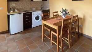 Une cuisine compacte équipée d’un four à micro-ondes, d’un évier et d’un lave-linge. On y trouve une table à manger avec des chaises et une petite plante en pot.