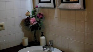 Une salle de bain avec un lavabo blanc, un miroir et un vase de fleurs.