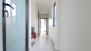 A long, narrow hallway with a glass door on the left, a fire extinguisher, and a window on the right. - Hello Dalat Hostel (Xuan Huong - Da Lat)