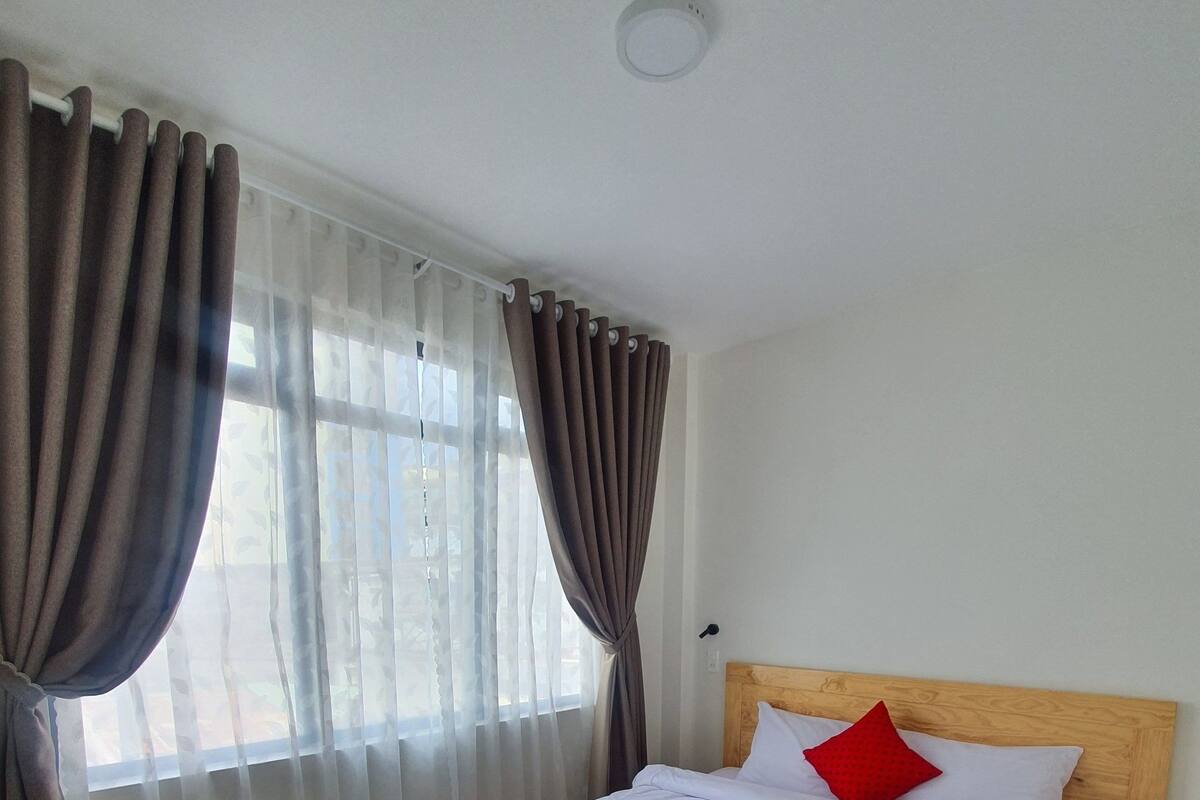 A bedroom with a wooden bed, white bedding, and a red pillow.