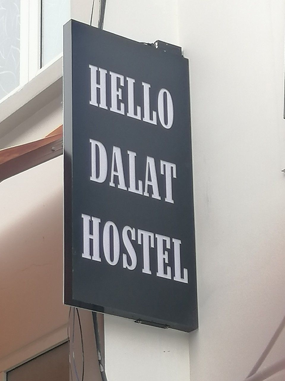A sign with the words 'HELLO DALAT HOSTEL' on a dark background.
