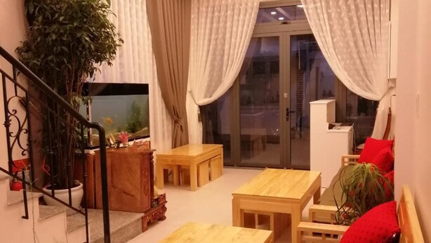 A cozy living room with a staircase, wooden furniture, and a large window with curtains. - Hello Dalat Hostel (Xuan Huong - Da Lat)