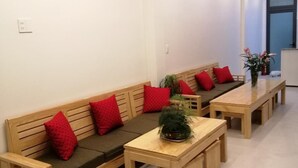 A modern living room with a wooden sofa, red cushions, a wooden coffee table, and a potted plant. - Hello Dalat Hostel (Xuan Huong - Da Lat)