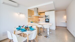 A modern kitchen with a central island, white bar stools, and a dining table set for four with blue plates. - Apartment in Alcudia Enjoy near the beach (Alcúdia)