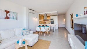 A modern living room with a white sofa, a dining table with chairs, and a kitchen area in the background. - Apartment in Alcudia Enjoy near the beach (Alcúdia)