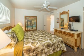 Ein Schlafzimmer mit Bett, Kommode, Deckenventilator, Gemälde und Fernseher.