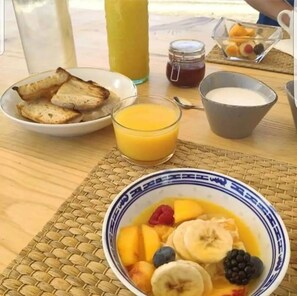 A breakfast table with toast, a glass of orange juice, a bowl of fruit, a jar of jam, and a cup of milk.