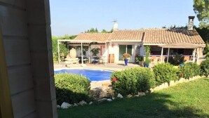 Vista des d'una porta cap a un pati posterior amb piscina, una terrassa coberta i una casa al fons.